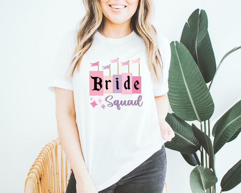 May include: White t-shirt with a pink and purple castle graphic and the text "Bride Squad" in black.