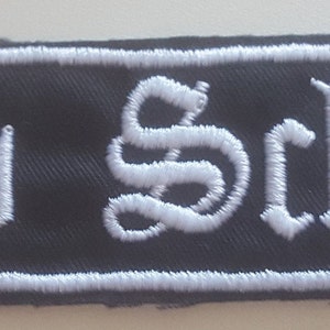 Könnte beinhalten: Schwarzer Stoff-Patch mit weiß gesticktem Text, der in gotischer Schrift "Old School" lautet.