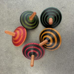 May include: Five wooden spinning tops with concentric circles in various colours: red and orange, black and red, green and black, and yellow and black. Each top has a natural wood peg.