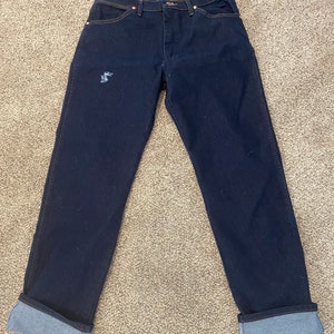 May include: A pair of dark blue denim jeans with cuffed hems. The jeans have a distressed look with a small hole on the left leg.