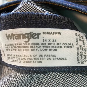 May include: A white Wrangler jeans care label with black text. The label says "13MAFPW - 34 X 34" and includes washing instructions. The label also says "Made in Nicaragua of US Fabric 76% Cotton 22% Polyester 2% Spandex Exclusive of Decoration."