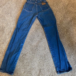May include: Blue denim jeans with a classic five-pocket design. The jeans have a straight leg cut and a brown leather patch on the back. The jeans are laid flat on a neutral-colored surface.