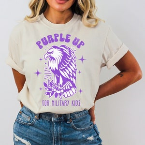 May include: A white t-shirt with a purple eagle graphic and the text "Purple Up for Military Kids".