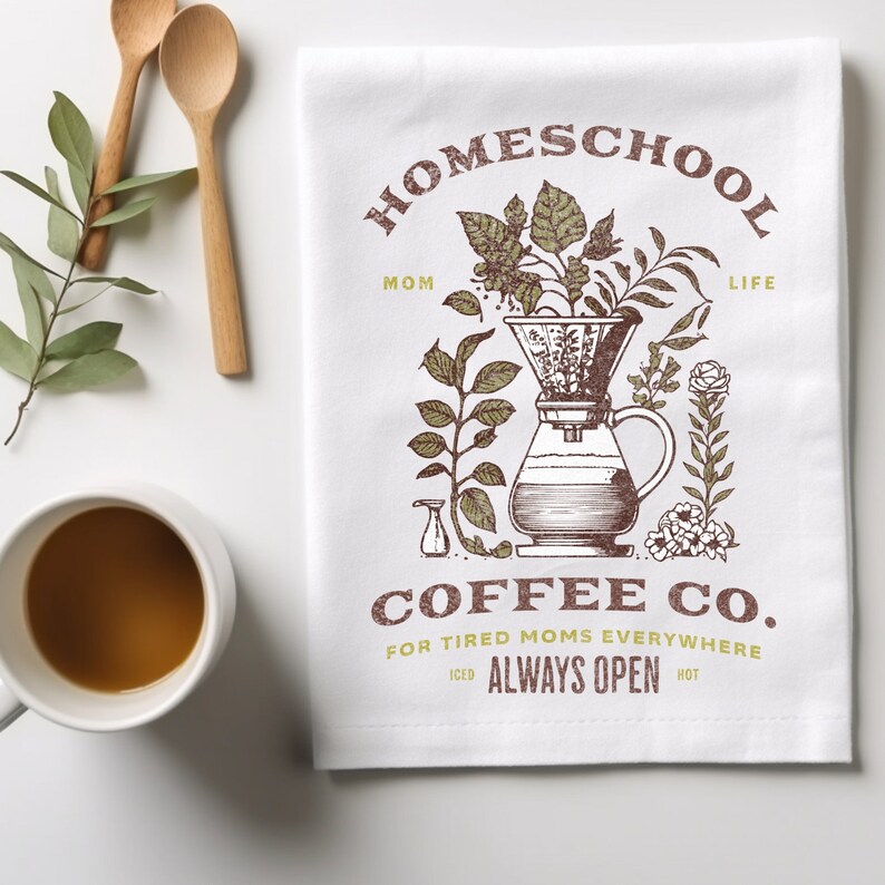 Puede incluir: Toalla de cocina blanca con una ilustraci&oacute;n marr&oacute;n de una cafetera con filtro y granos de caf&eacute;. El texto "HOMESCHOOL MOM LIFE" est&aacute; por encima de la ilustraci&oacute;n y "COFFEE CO. FOR TIRED MOMS EVERYWHERE" est&aacute; por debajo de la ilustraci&oacute;n. El texto "ICED ALWAYS OPEN HOT" est&aacute; debajo del nombre de la empresa de caf&eacute;.
