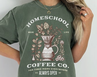 May include: Green t-shirt with a graphic of a coffee pot with plants and the text "Homeschool Mom Life Coffee Co. For Tired Moms Everywhere Iced Always Open Hot"
