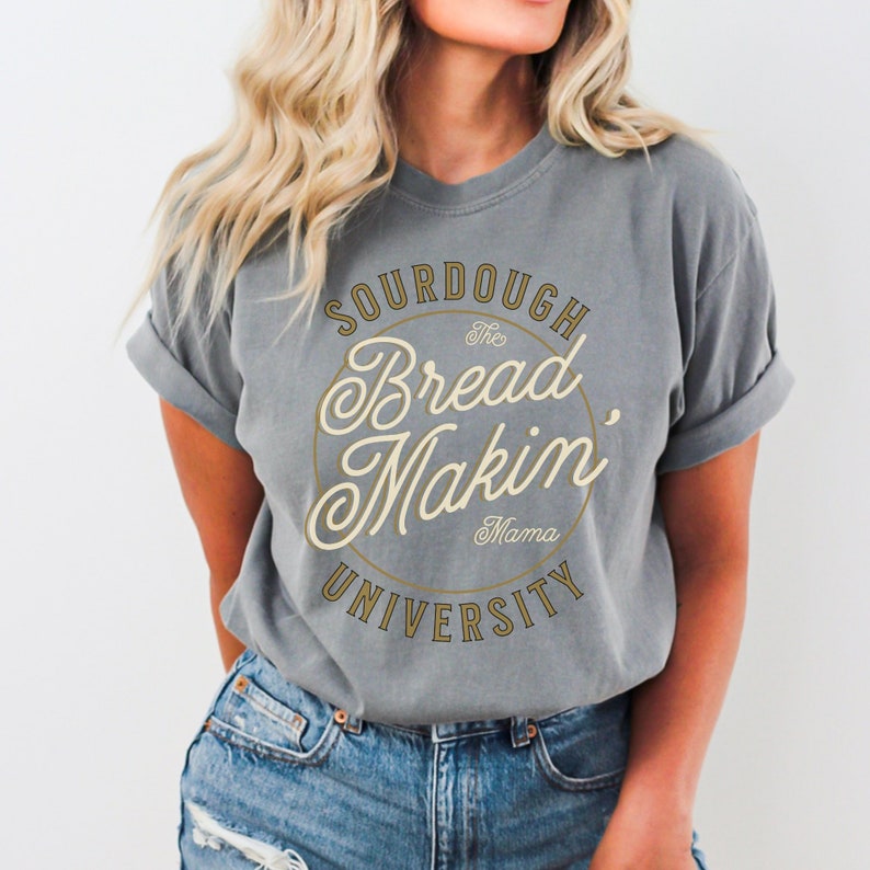 May include: A gray t-shirt with a gold circle graphic that says "The Bread Makin' Mama University" in a vintage font.