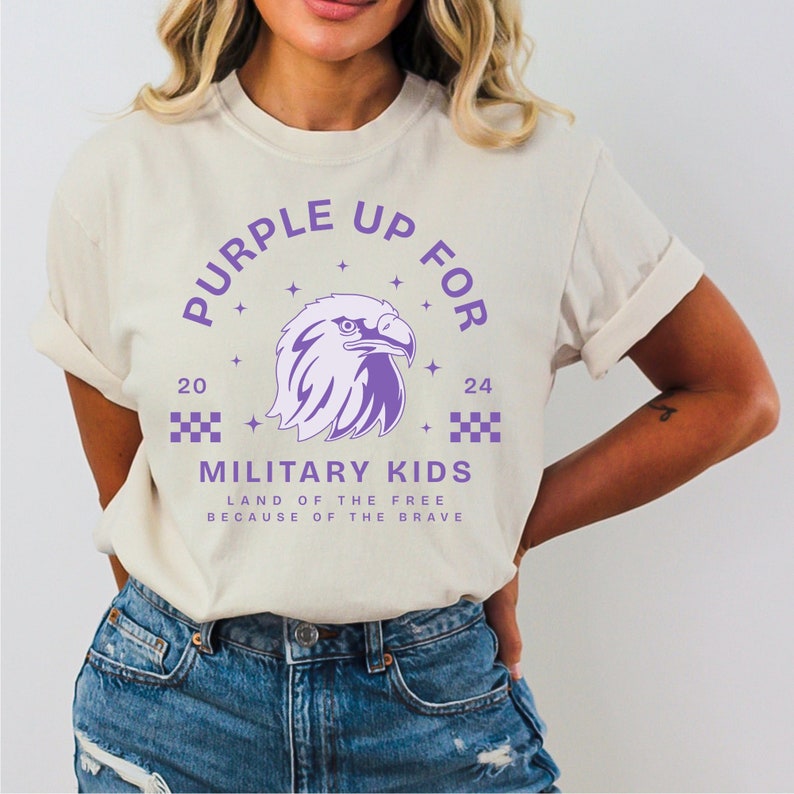 May include: A white t-shirt with a purple design featuring an eagle, stars, and the text "Purple Up For 20 24 Military Kids Land of the Free Because of the Brave".