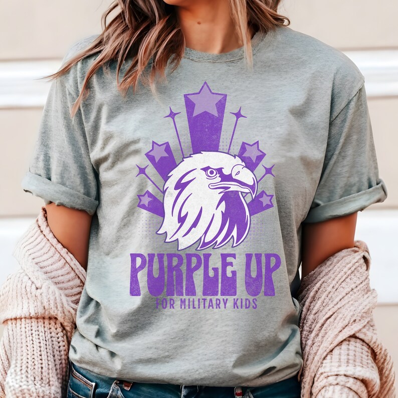 May include: Purple Up for Military Kids t-shirt featuring a purple eagle graphic and stars. The shirt is on a grey background.