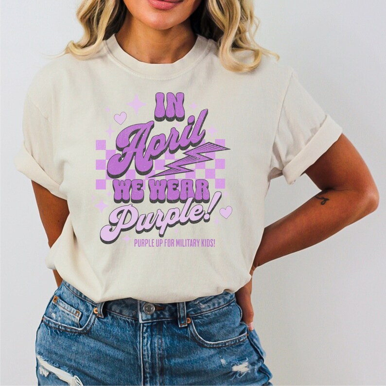 May include: A white t-shirt with a purple graphic that says "In April We Wear Purple!" with a chequered background and lightning bolt. The text "Purple Up for Military Kids!" is also included.
