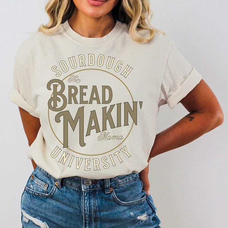May include: A white t-shirt with a brown circle graphic that says "The Bread Makin' Mama University" in a vintage font.