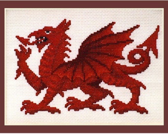 Puede incluir: Punto de cruz de un dragón rojo sobre fondo blanco, enmarcado en un borde marrón. El dragón está detallado con alas, garras y una cola enroscada. La labor de aguja es visible, creando un efecto texturizado.