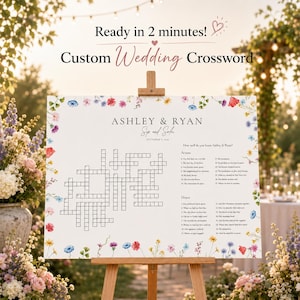 Könnte beinhalten: Ein individuelles Hochzeitskreuzworträtsel auf einer Holzstaffelei. Das weiße Schild zeigt die Namen "Ashley & Ryan" und ein Kreuzworträtselgitter, umrahmt von bunten floralen Akzenten. Der Text oben lautet "Fertig in 2 Minuten!" und "Individuelles Hochzeitskreuzworträtsel."