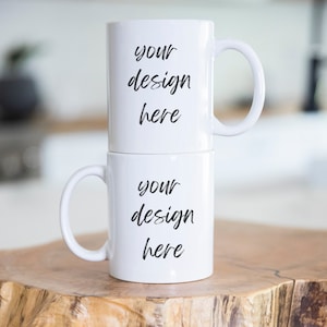 Könnte beinhalten: Zwei weiße Keramikbecher, die übereinander gestapelt sind. Die Becher haben schwarzen Text, der auf beiden Seiten "your design here" lautet.