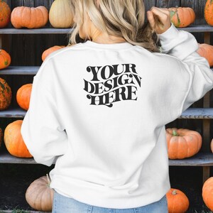 May include: White sweatshirt with the text "YOUR DESIGN HERE" printed on the back. The sweatshirt is in front of a wooden shelf with pumpkins.