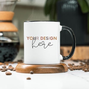May include: White ceramic mug with a black rim and handle. The mug has the text "YOUR DESIGN here" printed on the front in a black script font.