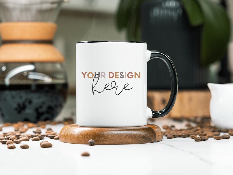 May include: White ceramic mug with a black rim and handle. The mug has the text "YOUR DESIGN here" printed on the front in a black script font.