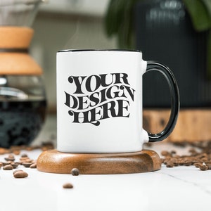 May include: White ceramic mug with a black rim and handle. The mug has the text "YOUR DESIGN HERE" printed in black on the front.