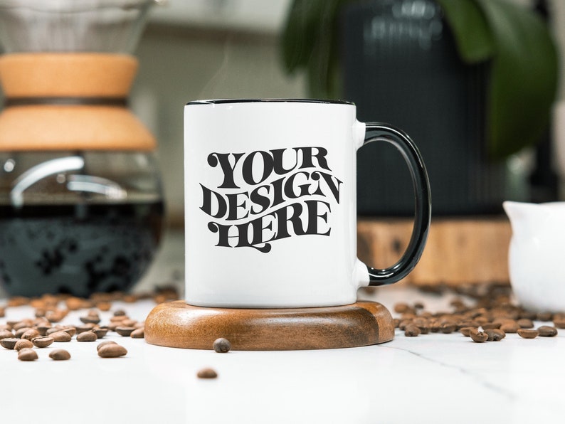 May include: White ceramic mug with a black rim and handle. The mug has the text "YOUR DESIGN HERE" printed in black on the front.