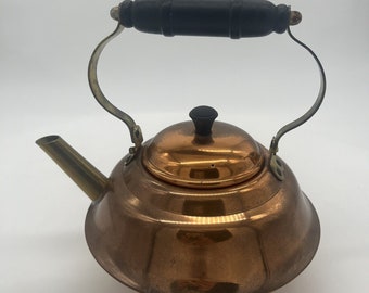 May include: A copper tea kettle with a wooden handle and a brass spout. The kettle has a shiny, polished finish.