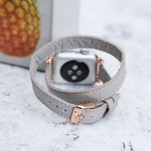 May include: A gray leather Apple Watch band with a rose gold buckle. The band is double-wrapped and has a minimalist design.