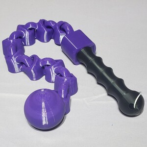 May include: A 3D-printed purple and black object with a chain-like structure and a handle. The chain connects to a purple sphere. The handle is black with a textured grip. The object is on a white surface.