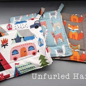 May include: Three square quilted pot holders with different patterns. One has a camping theme with tents, a camper, and a campfire. Another has llamas, and the third has foxes wearing glasses and bandanas. The text "Unfurled Hands" is at the bottom.