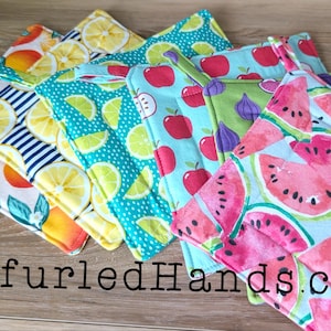 May include: A selection of square fabric pot holders with fruit designs, such as lemons, oranges, apples, figs, and watermelons. The pot holders are arranged in a fan shape, with the text "UnfurledHands.com" at the bottom.