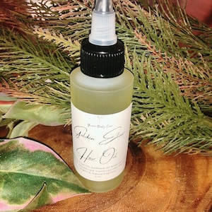 May include: A clear glass bottle with a black cap and a dropper top. The bottle is filled with a yellow liquid and has a white label that reads "Golden Elixir Hair Oil". The label also includes the text "You're Body Care" and a list of ingredients.