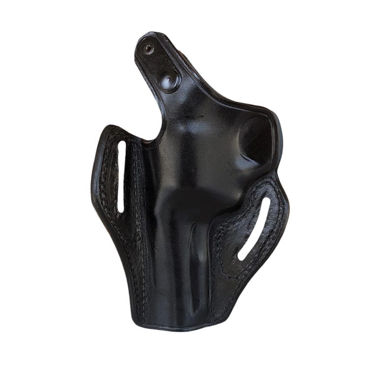 May include: A black leather holster with a glossy finish. The holster has a molded shape with stitched edges and several openings. A snap closure is visible at the top.