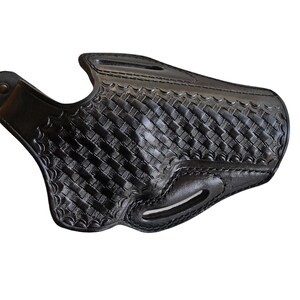 May include: A black leather holster with a basketweave pattern. The holster has a curved shape with a belt loop and a snap closure. The edges are stitched, and the leather appears to be thick and durable.