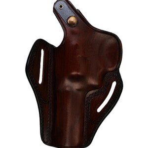 May include: A dark brown leather holster with a glossy finish. The holster features a curved design with stitched edges and two vertical slots. A metal rivet and a brass button secure the top flap.