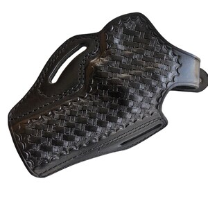 May include: Black leather holster with a basketweave pattern. The holster features a belt loop, a molded shape, and stitched edges. The design includes an opening for a firearm and a handle cutout.