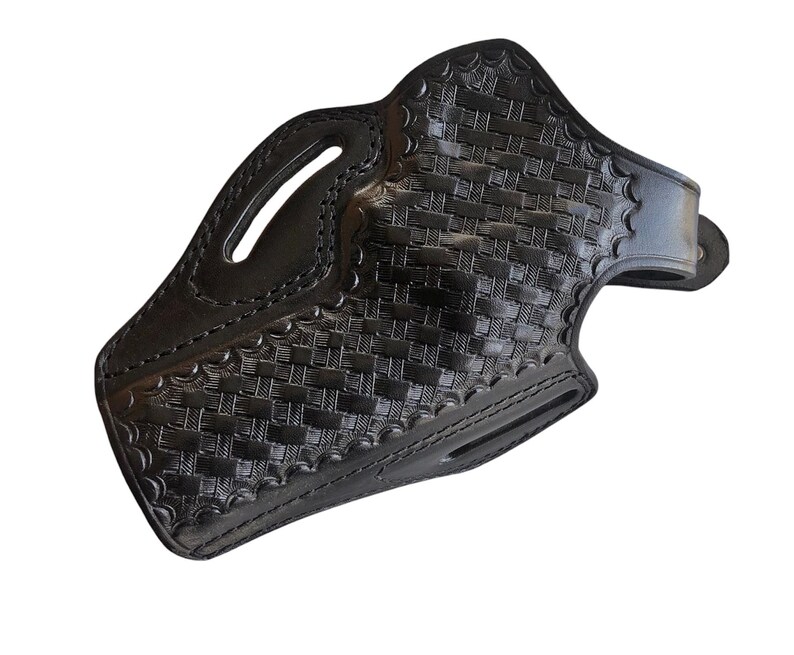 May include: Black leather holster with a basketweave pattern. The holster features a belt loop, a molded shape, and stitched edges. The design includes an opening for a firearm and a handle cutout.
