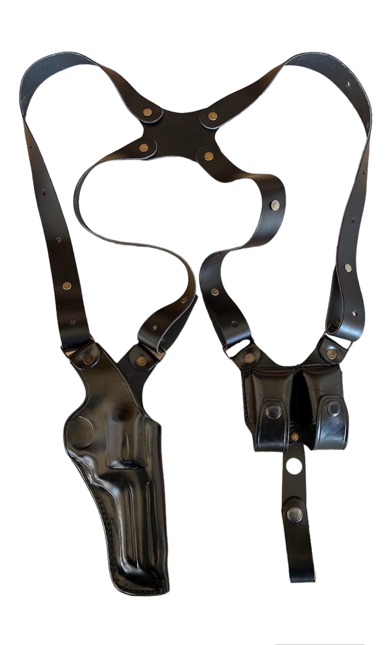 Peut inclure: Un holster d'&eacute;paule en cuir noir avec un &eacute;tui &agrave; pistolet et deux pochettes &agrave; magazines. Le holster est dot&eacute; de sangles r&eacute;glables et d'&eacute;l&eacute;ments m&eacute;talliques. La conception comprend un &eacute;tui vertical pour un pistolet et deux pochettes pour les chargeurs.