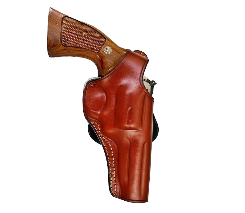 May include: A brown leather holster for a revolver. The holster has a stitched design and a flap that covers the trigger guard.