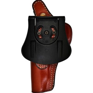 May include: A brown leather holster with a black plastic belt clip. The holster has a stitched design and a flap that covers the top of the gun.