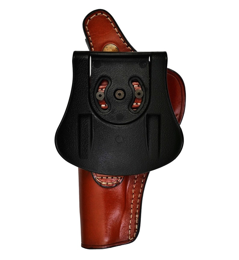 May include: A brown leather holster with a black plastic belt clip. The holster has a stitched design and a flap that covers the top of the gun.
