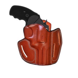 Peut inclure: Un revolver noir avec une poignée texturée est partiellement inséré dans un étui en cuir beige. L'étui présente des contours moulés pour l'arme à feu, des coutures contrastantes blanches sur les bords et deux fentes verticales sur les côtés.