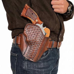 May include: A brown leather holster with a woven pattern, holding a silver and wood-handled revolver. The holster is worn on a brown leather belt over blue jeans. The revolver's wooden grip is visible.