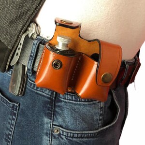 May include: A brown leather holster with two compartments for carrying small items. The holster is worn on a person's belt and has a silver metal snap closure.