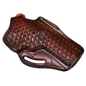 May include: A brown leather holster with a basketweave pattern. The holster has a curved shape with a belt loop and a cutout for the trigger guard. The leather is a rich, dark brown color with visible stitching.