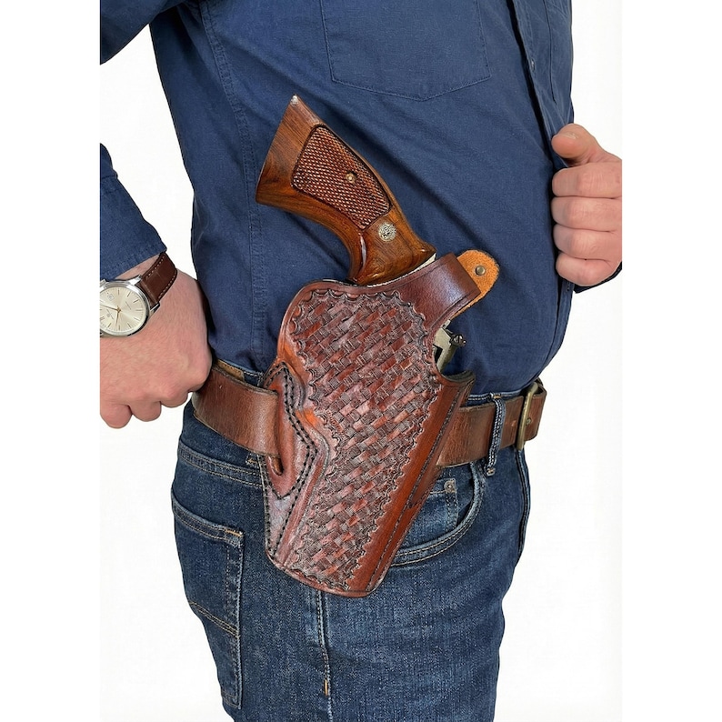 May include: A brown leather holster with a woven pattern, holding a revolver with a wooden grip. The holster is attached to a brown leather belt worn with blue jeans and a blue shirt.