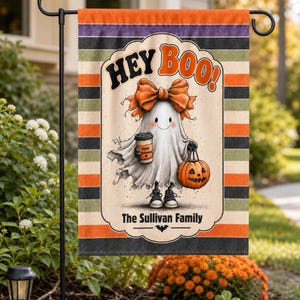 May include: A rectangular garden flag featuring horizontal stripes in orange, black, and muted green. The centre displays a ghost character wearing a large orange bow, holding a coffee cup and a jack-o'-lantern, with the text HEY BOO! and The Sullivan Family.