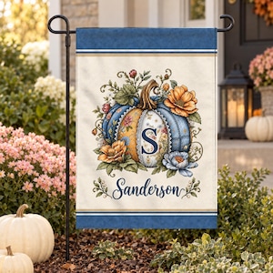 May include: A rectangular garden flag with a cream-colored center and dark blue borders. The design features a central pumpkin decorated with floral patterns, a large letter S, and the name Sanderson in blue script, surrounded by autumn flowers.