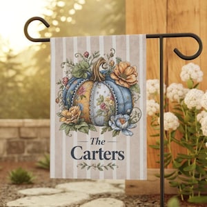 May include: A rectangular garden flag featuring a vertical beige and white striped background. The center displays a large pumpkin with blue and yellow floral patterns, surrounded by orange and blue flowers. The text reads The Carters.