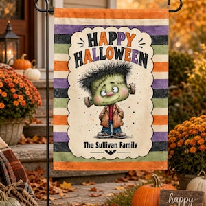 May include: A rectangular garden flag featuring horizontal stripes in orange, purple, black, and green. The centre displays a cartoon Frankenstein monster with the text Happy Halloween above and The Sullivan Family below a small black bat icon.