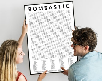 May include: A black framed poster with the word "BOMBASTIC" at the top. The poster has a grid of small black dots and a list of words at the bottom. A man and woman are holding the poster.