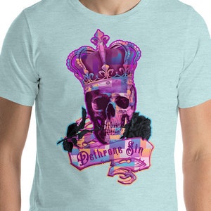 Könnte beinhalten: Ein hellblaues T-Shirt mit einem Motiv eines Schädels, der eine lila und rosafarbene Krone trägt. Der Schädel hält eine Rose und ein Banner mit der Aufschrift "Dethrone Sin".