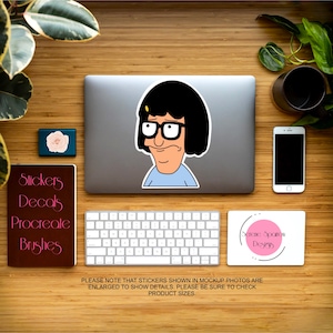 Puede incluir: Una ilustraci&oacute;n digital de un personaje de dibujos animados con cabello negro, gafas y una camisa azul. La imagen es una pegatina para usar con una computadora port&aacute;til, un tel&eacute;fono u otra superficie lisa. El texto "Serene Sparrow Designs" es visible en la imagen.