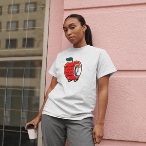 May include: White t-shirt with a red apple graphic. The apple has a face and is driving a car. The text on the shirt reads "My other car is a box truck brand".